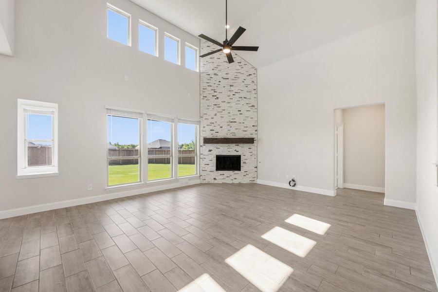 Open living room with two-story ceiling, floor-to-ceiling stone fireplace, ceiling fan, and wood-look tile floors Open living room with two-story ceiling, floor-to-ceiling stone fireplace, ceiling fan, and wood-look tile floors