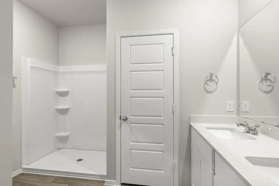Image of a primary bathroom with light grey walls, a white jack and jill vanity, a large mirror and a white standing shower Image of a primary bathroom with light grey walls, a white jack and jill vanity, a large mirror and a white standing shower