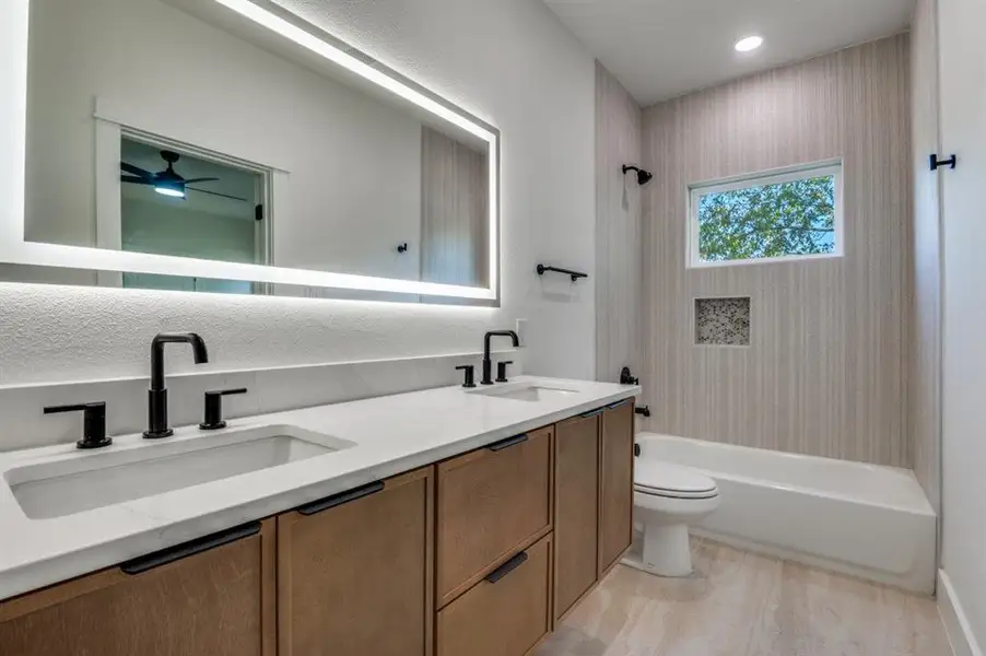 Full bathroom featuring double vanity, shower / bath combination, a ceiling fan, and light wood-style floors