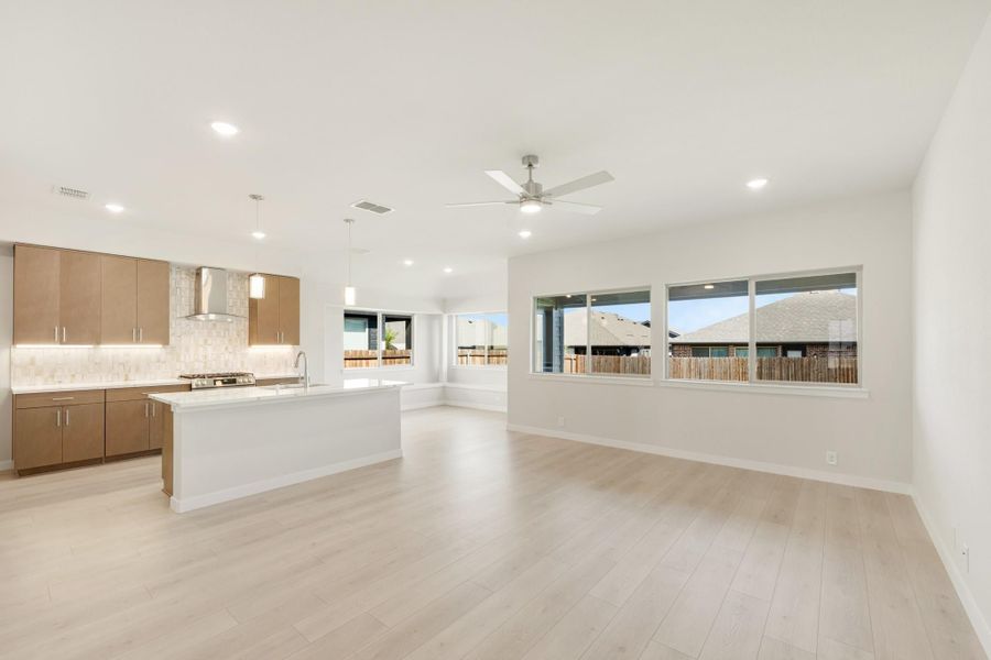 Open-concept kitchen and living area with white island, brown cabinets, and light wood floors