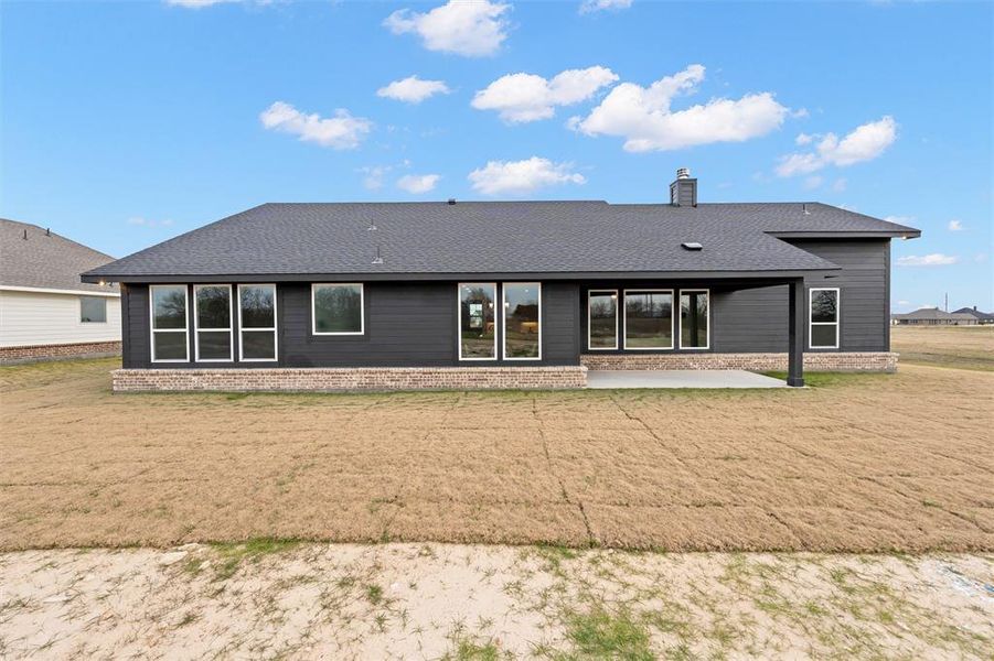 Back of house featuring a patio, a shingled roof, a lawn, a chimney, and brick siding