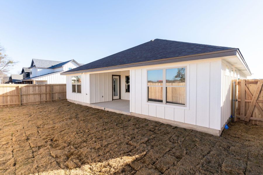 Rear view of property featuring a patio area, board and batten siding, roof with shingles, a fenced backyard, and a gate