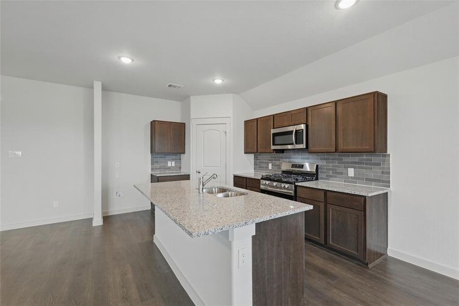 Kitchen with light stone counters, stainless steel appliances, dark wood finished floors, and a kitchen island with sink Kitchen with light stone counters, stainless steel appliances, dark wood finished floors, and a kitchen island with sink