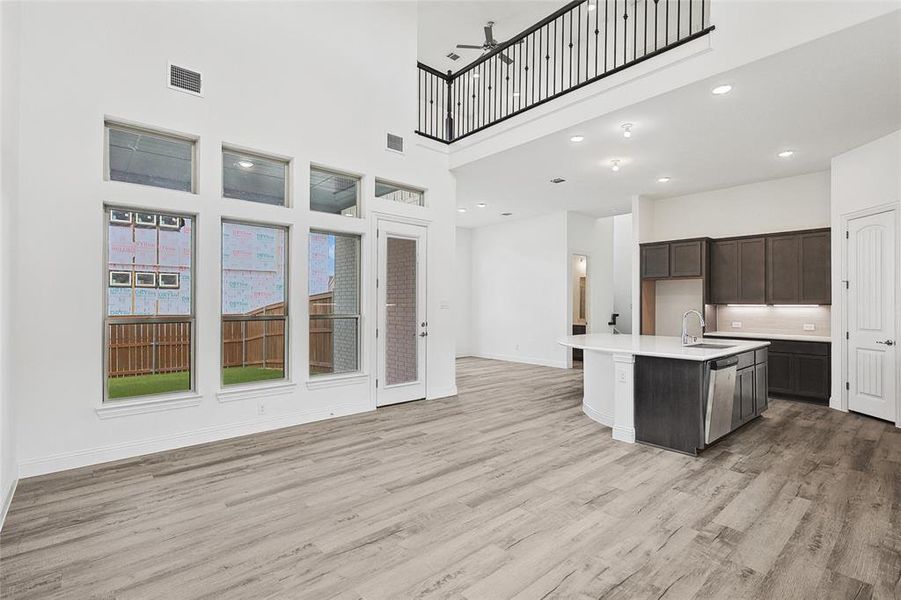 Kitchen with dishwasher, dark brown cabinetry, sink, light wood-type flooring, and a kitchen island with sink