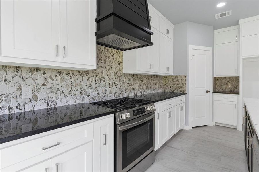 Kitchen with stainless steel range with gas stovetop, custom range hood, white cabinets, and recessed lighting