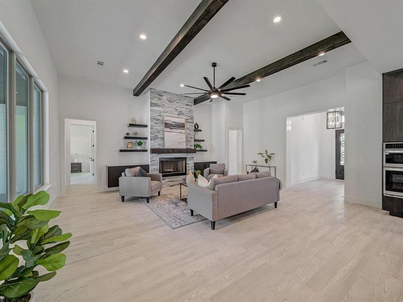 Living area with beamed ceiling, a towering ceiling, a tile fireplace, a ceiling fan, and light wood-style flooring