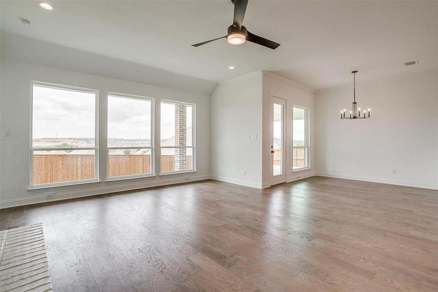 Spare room featuring ceiling fan with notable chandelier, crown molding, light hardwood / wood-style flooring, and a healthy amount of sunlight