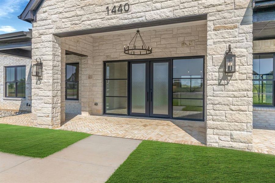Property entrance with  custom iron and glass entry doors, stone siding, and a patio area