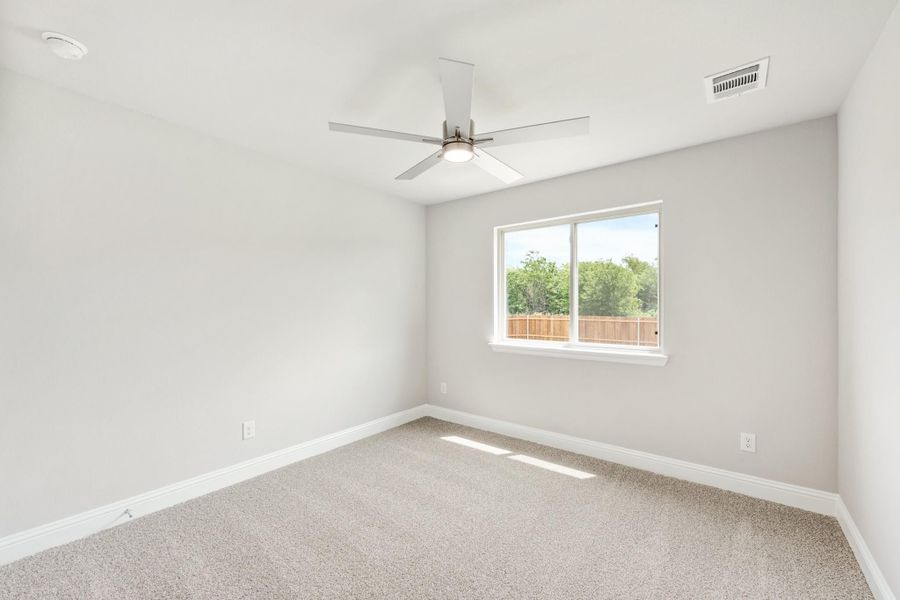 Empty bedroom with carpet flooring, ceiling fan, and a window overlooking a fenced backyard Empty bedroom with carpet flooring, ceiling fan, and a window overlooking a fenced backyard