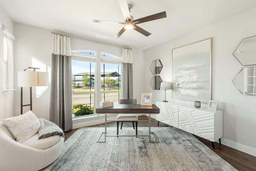 Home office with dark wood desk, hardwood floors, ceiling fan, and large arched window with gray curtains