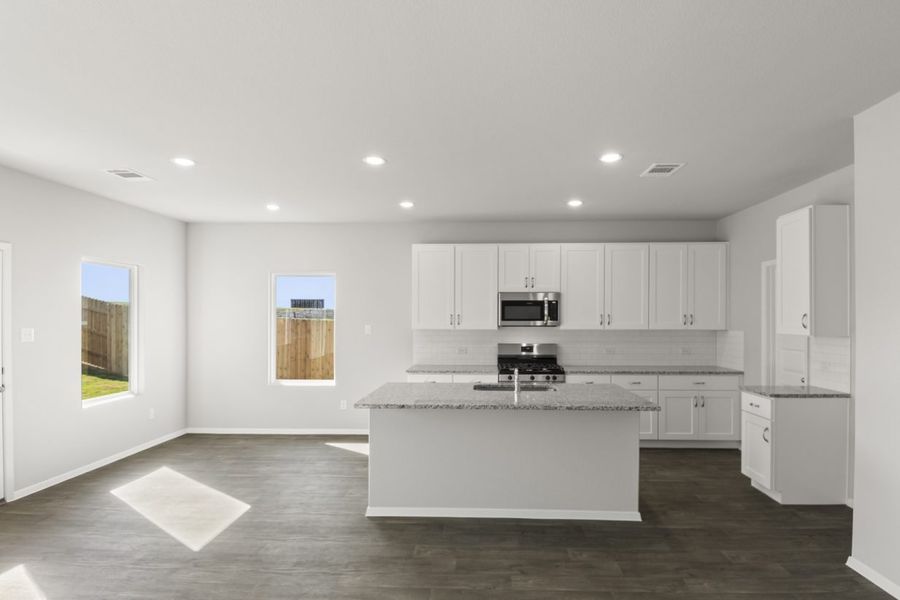 Image of a kitchen with a white center island and cabinets with granite countertops and black appliances with a dining area to the left