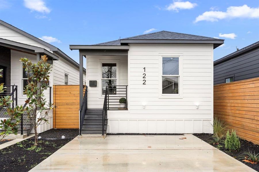 This modern, beautifully designed home features a sleek white exterior, a welcoming front porch, stylish black railing, and a private driveway, all complemented by contemporary landscaping.