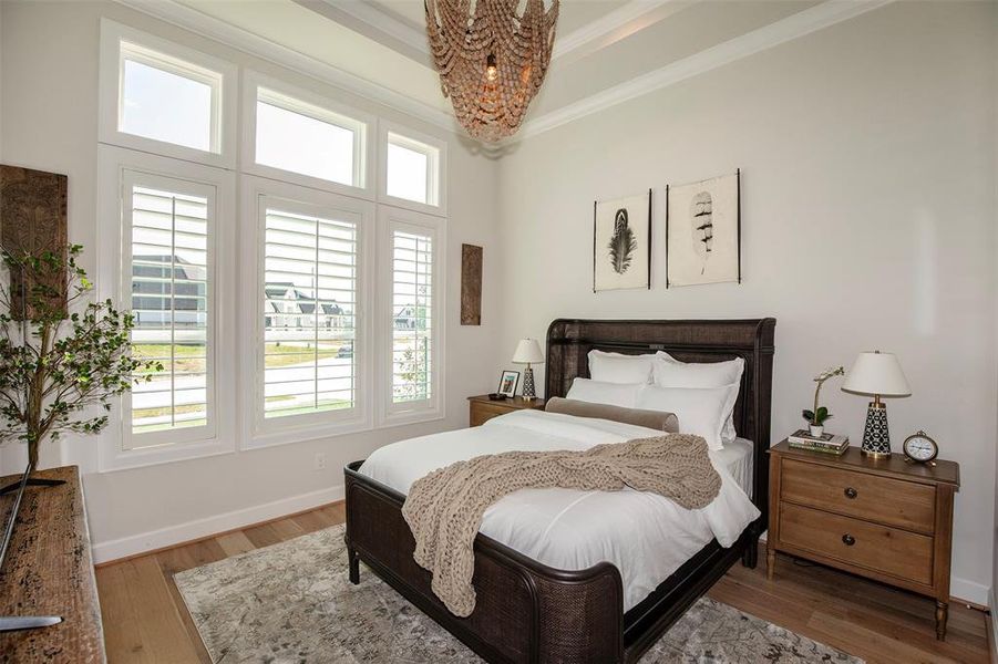 This bedroom is bright and inviting, featuring large windows with plantation shutters that allow plenty of natural light. It has a cozy, well-dressed bed, elegant decor with minimalist artwork, and wooden furniture, creating a warm and comfortable atmosphere.