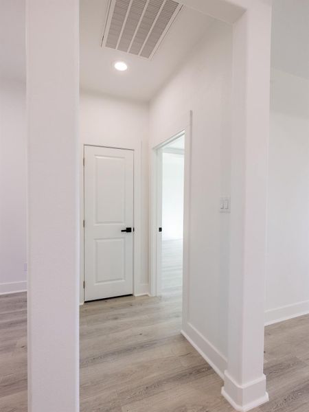 This photo shows a bright, modern hallway with light wood floors and white walls. It features a clean design with a white door and open doorway, creating a welcoming and spacious feel.