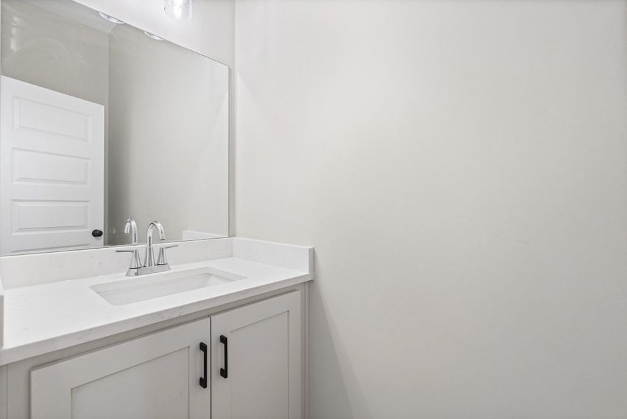Vanity featuring a white countertop with an integrated sink, chrome faucet, and white cabinetry with black hardware Vanity featuring a white countertop with an integrated sink, chrome faucet, and white cabinetry with black hardware