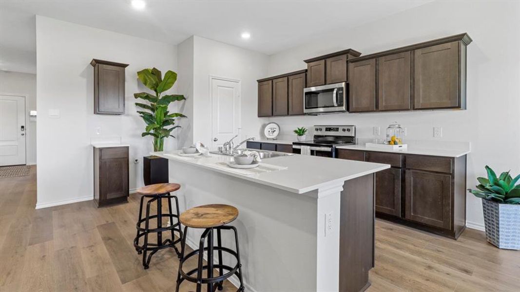Kitchen with dark wood finish cabinetry, stainless steel appliances, a kitchen island with sink, a breakfast bar area, and light wood-style floors