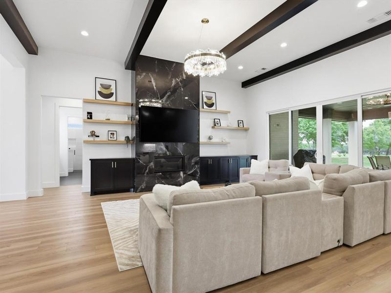 Spacious living area featuring a vaulted ceiling with dark wood beams, a striking black marble-look fireplace surround, and wood-finish flooring