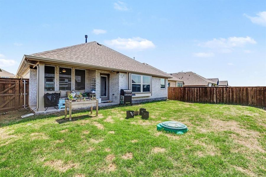 Expansive backyard featuring a lush lawn, privacy fencing, and a covered patio area
