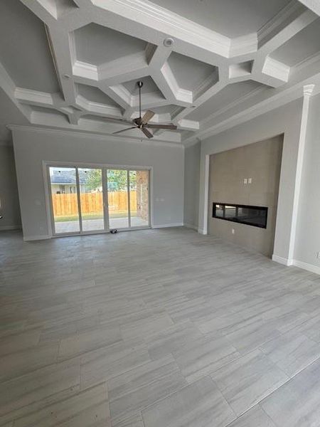 Unfurnished living room with coffered ceiling, ornamental molding, a glass covered fireplace, beamed ceiling, and ceiling fan