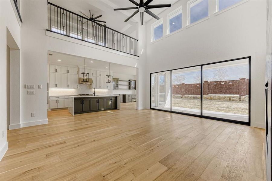 Unfurnished living room featuring ceiling fan, light wood-style floors, and a high ceiling