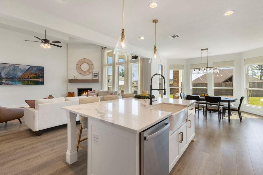 This open-concept home features a bright kitchen with a large island and modern fixtures, seamlessly flowing into a cozy living area with a fireplace. The dining space offers abundant natural light from multiple windows, creating a welcoming and airy ambiance.