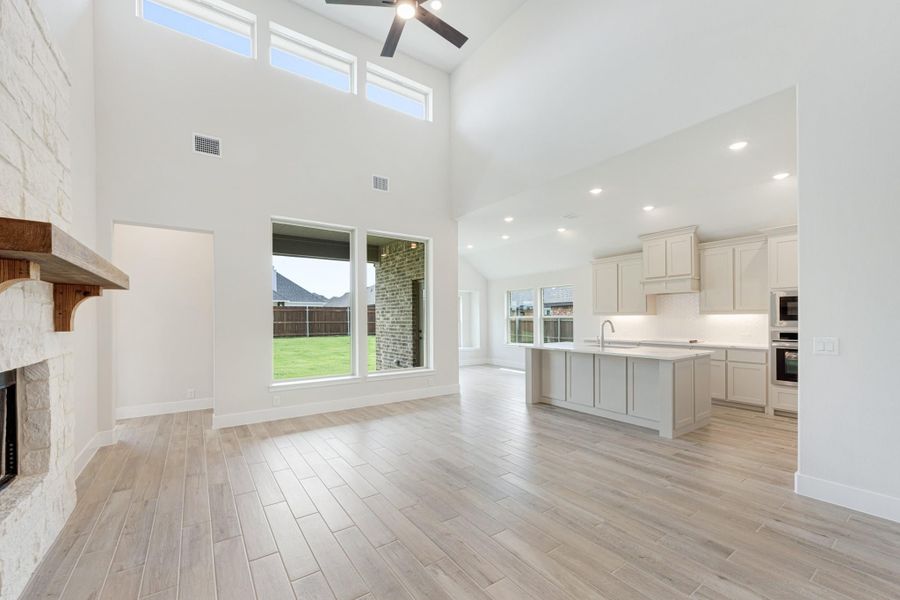 Open-concept living area with stone fireplace, high ceilings, and kitchen island visible in background