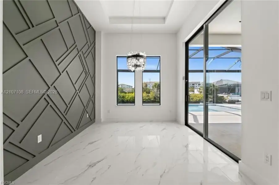 Geometric millwork accent wall, high-gloss stone-finish flooring, tray ceiling with crystal-style chandelier, and floor-to-ceiling sliding glass doors