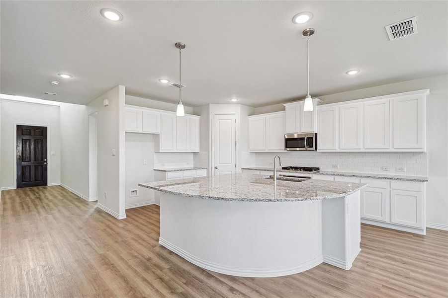 Kitchen with light stone counters, white cabinets, a center island with sink, and light wood-type flooring