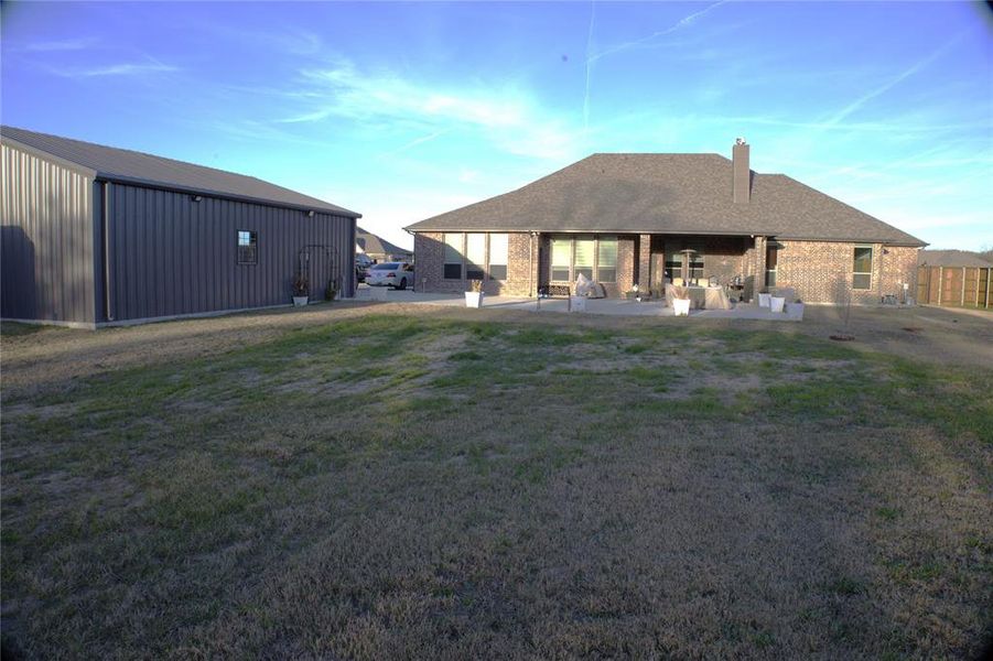 New Addition - Back of house featuring brick siding, an outdoor structure, a patio, a yard, and a chimney