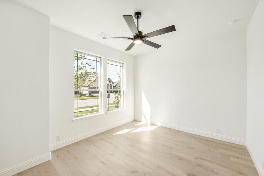 Empty room with light wood floors, white walls, ceiling fan, and two windows with neighborhood view