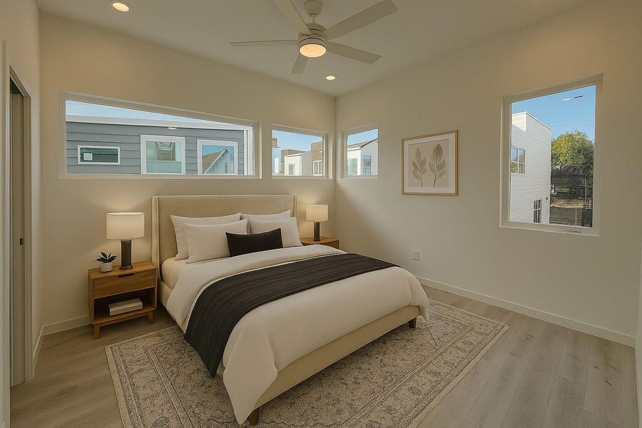This cozy bedroom features large windows for ample natural light, a comfortable bed with neutral bedding, stylish wooden nightstands, and a ceiling fan, all set on light wood flooring for a modern touch.