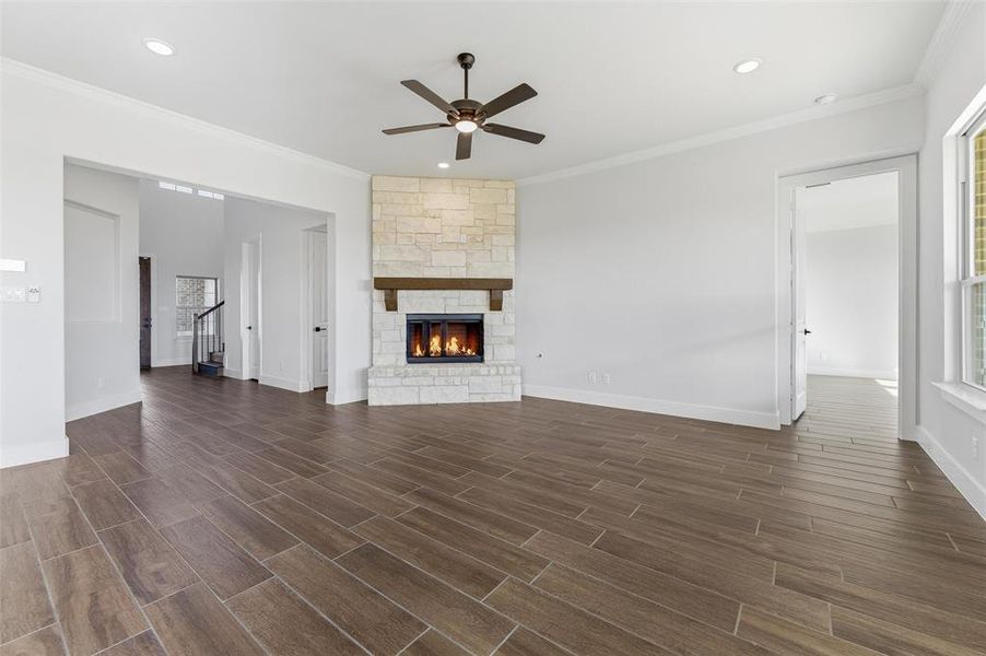 Unfurnished living room with a stone fireplace, recessed lighting, ceiling fan, wood finish floors, and ornamental molding