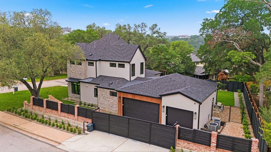 Contemporary residence featuring a light-colored stucco and stone facade, dark-framed windows, and a multi-level asphalt shingle roof