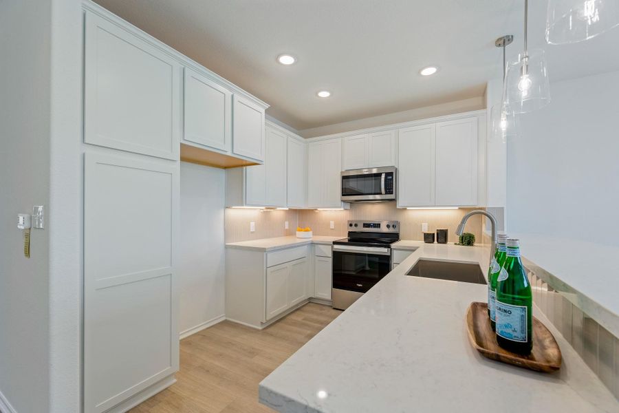 Kitchen featuring stainless steel appliances, light stone countertops, white cabinets, light wood-type flooring, and hanging light fixtures