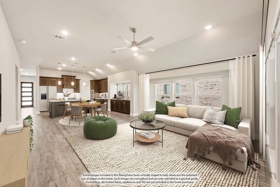 Open-concept living room with vaulted ceiling, hardwood floors, and kitchen visible in background