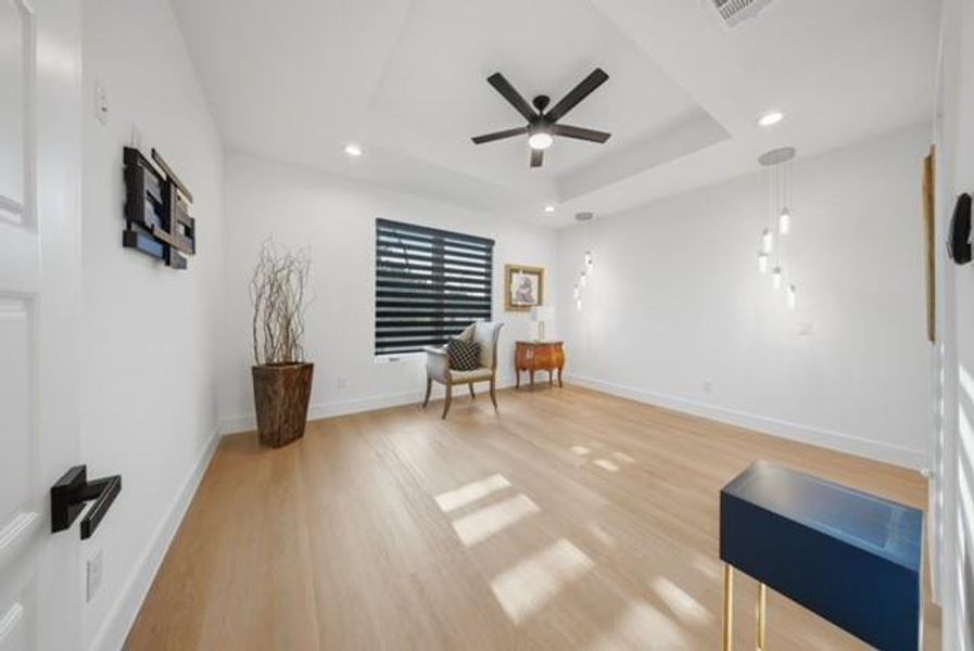 Spacious interior featuring light wood-finish flooring, a tray ceiling with a ceiling fan, recessed lighting, and multiple pendant light fixtures