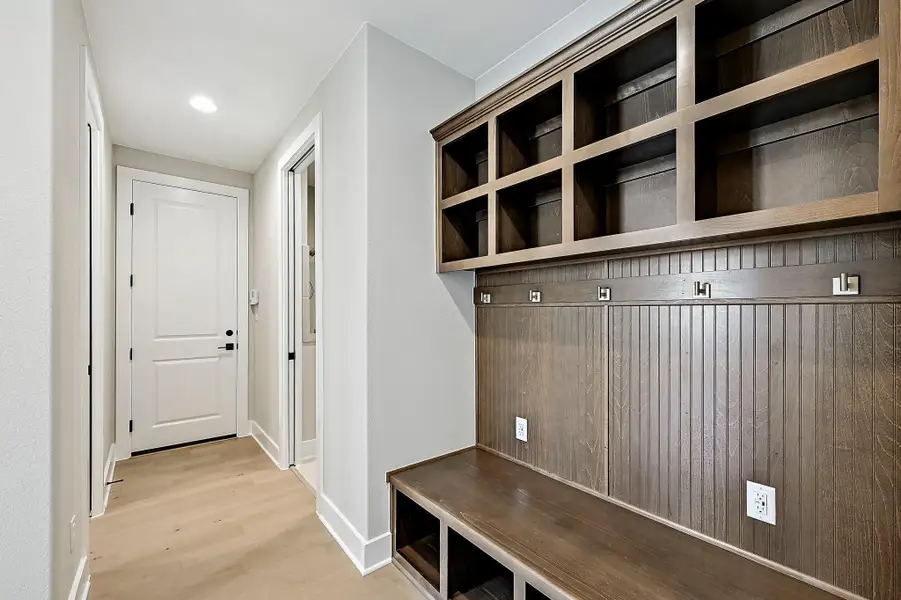 A built-in wooden mudroom bench with cubbies and overhead shelving organizes this home's garage entryway.