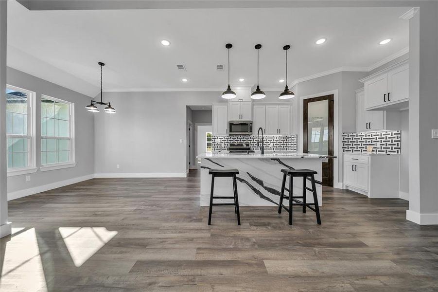 Kitchen featuring a kitchen island with sink, white cabinets, and decorative light fixtures