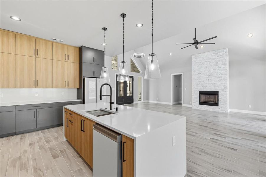 Kitchen with light brown cabinets, wood tiled floors, hanging light fixtures, light stone counters, and a kitchen island with sink Kitchen with light brown cabinets, wood tiled floors, hanging light fixtures, light stone counters, and a kitchen island with sink