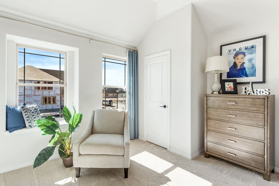 Bedroom sitting area with vaulted ceiling, window seat, accent chair, and wood dresser on carpet flooring