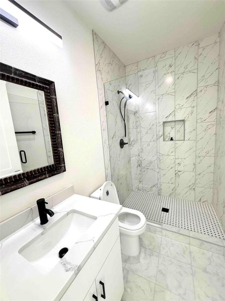 Full bathroom featuring vanity, a marble finish shower, and light marble finish floors