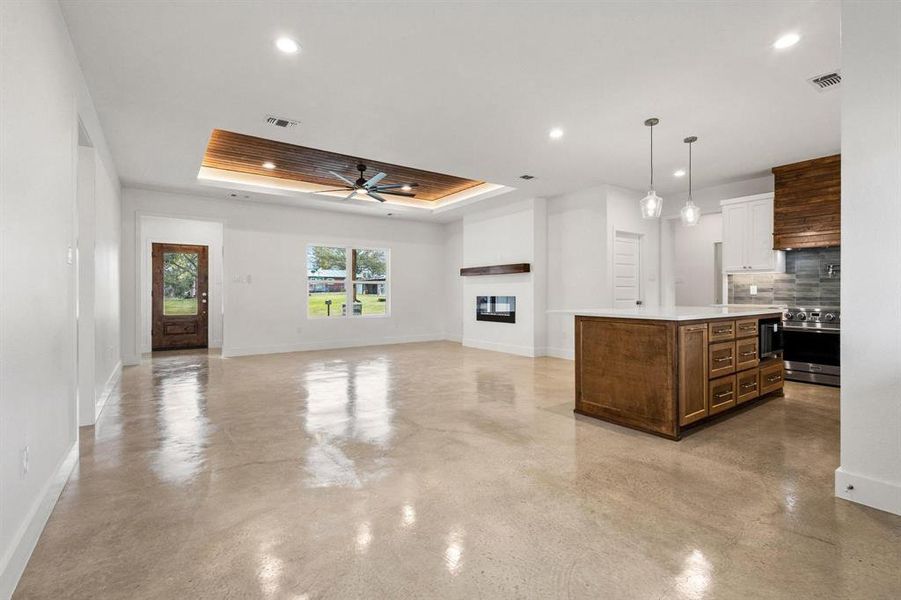 Kitchen featuring a glass covered fireplace, pendant lighting, a raised ceiling, a kitchen island, and open floor plan
