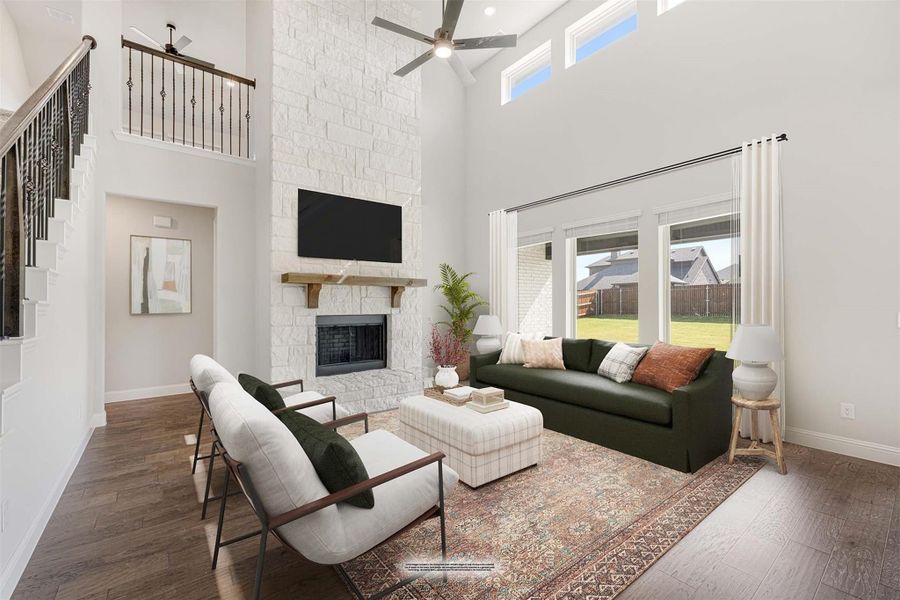 Living room with two-story ceiling, floor-to-ceiling stone fireplace, hardwood floors, and ceiling fan