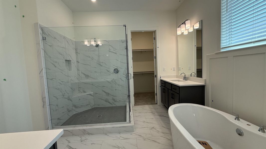 Bathroom featuring vanity, a freestanding bath, a marble finish shower, a walk in closet, and light marble finish flooring