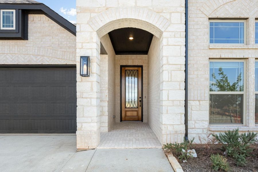 Home entrance with stone arch, wood and iron front door, and dark garage door nearby