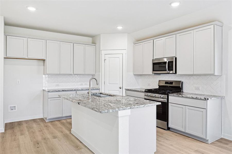 Kitchen with light stone countertops, stainless steel appliances, light hardwood / wood-style floors, and sink