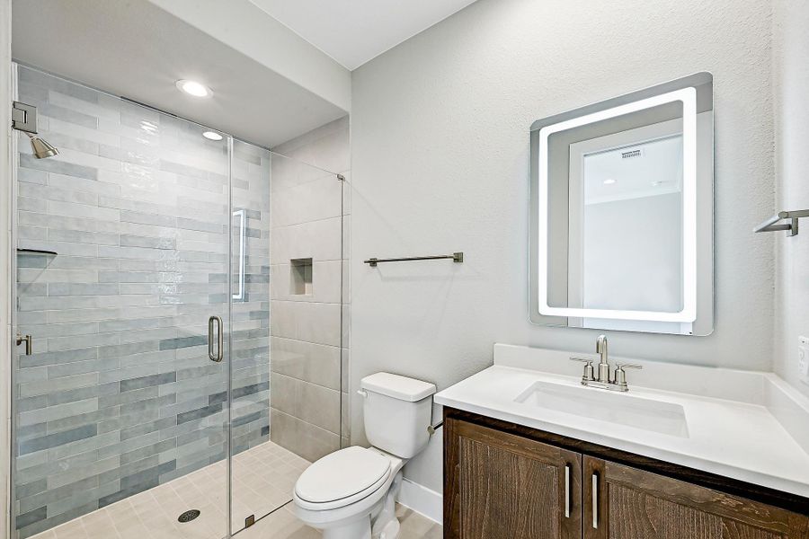 A well-appointed bathroom features a glass-enclosed shower and a modern vanity with an illuminated mirror.