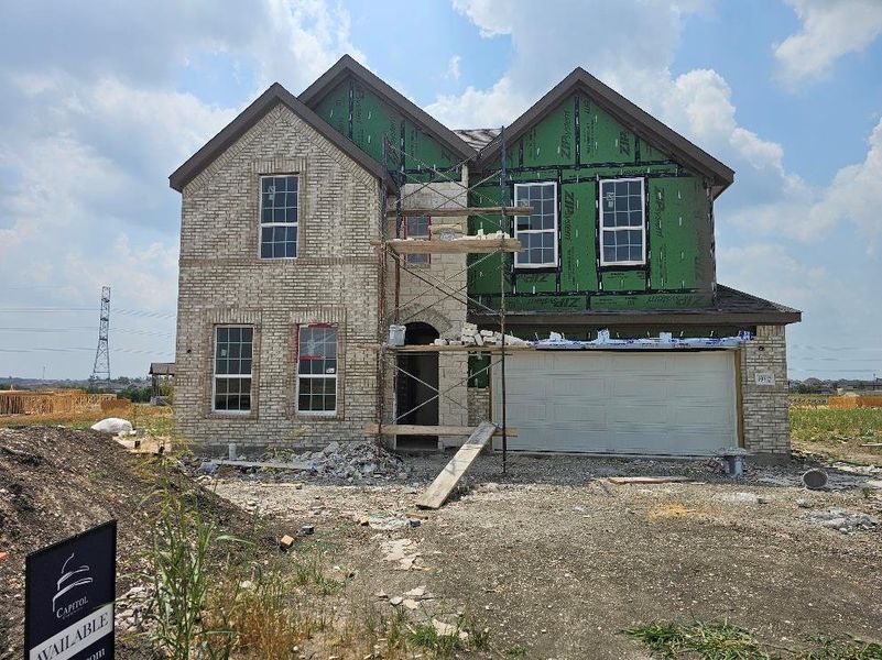 Property in mid-construction featuring brick siding, an attached garage, and driveway Property in mid-construction featuring brick siding, an attached garage, and driveway