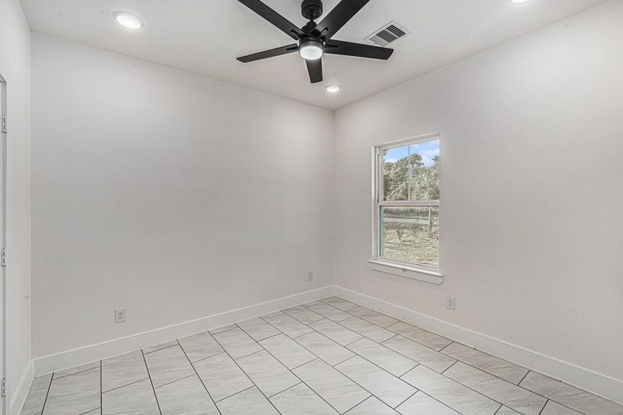 This room features clean, white walls and tiled flooring, offering a modern and minimalistic look. It includes a window for natural light and a ceiling fan with lights, perfect for comfort and versatility.
