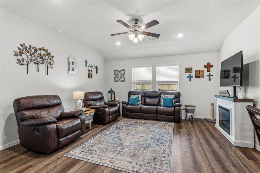 Living room with ceiling fan, vaulted ceiling, dark wood-style floors, a glass covered fireplace, and recessed lighting
